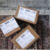 Three labeled delivery boxes placed on a decorative rug over a wooden floor.